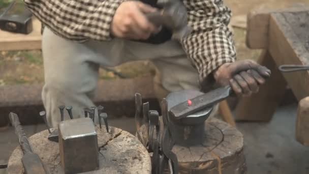 铁匠在露天车间手工制作的金属制品的生产过程中。铁匠用锤子敲金属。一个拿着红热钢坯的铁匠的手 — 图库视频影像
