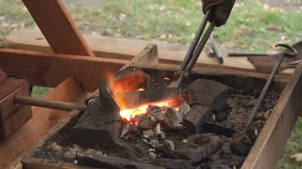 The blacksmith holds the billet over hot coals in a clay oven. blacksmith heating iron metal sword manufacturing marching forge — Stock Video