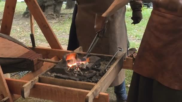 Kowala posiada kęsów na rozżarzonych węglach w glinianym piecu. Kowal ogrzewanie metalowy miecz żelaza, produkcji kuźni marszowy — Wideo stockowe