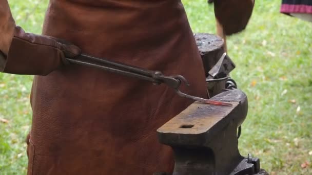 Коваль у виробництві металевих виробів ручної роботи на майстерні Онеїр. Коваль завдає удару молотком по металу. Руки коваля в шкіряних рукавичках з червоно-гарячою заготовкою — стокове відео