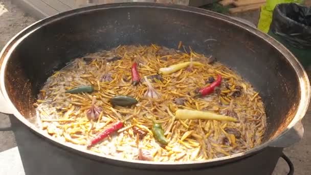 Uzbek national dish pilaf in a large cast-iron cauldron on the fire, sliced yellow carrots, added barberry, whole of garlic and red green and yellow chili pepper, boiling, rice, lamb, mutton fat, the — Stock Video