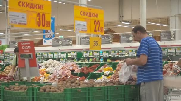 МОСКВА 29 СЕНТЯБРЯ 2018 г.: Люди покупают продукцию в Ашане. Мужчина и женщина собирают овощи в пластиковых пакетах со стойки в гипермаркете Ашан. Плоское видео — стоковое видео