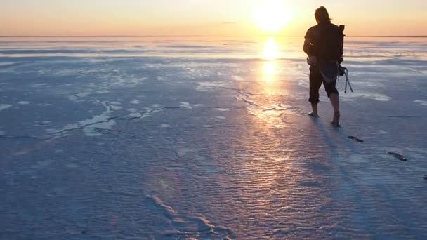 Silhouette di un uomo che cammina sulla superficie di un lago salato contro il sole al tramonto. Fotografo va a scattare il tramonto al lago salato su sfondo tramonto per godere colorato cielo tramonto. Salina — Video Stock