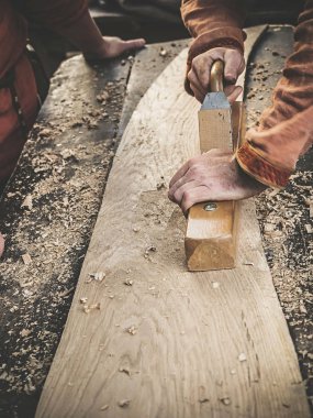 Uçakla bir ahşap çalışma Ortaçağ pamuklu giysiler içinde bir marangoz. Adam el ile bir ahşap tahta bir uçakla Hews. İnşaat ahşap kabuk