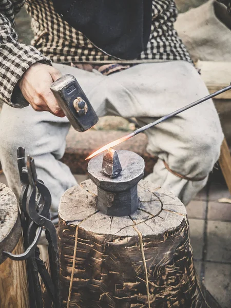 The blacksmith in the production process of metal products handmade on the openair workshop. Blacksmith strikes with a hammer on metal. Hands of a blacksmith with red-hot billet close up