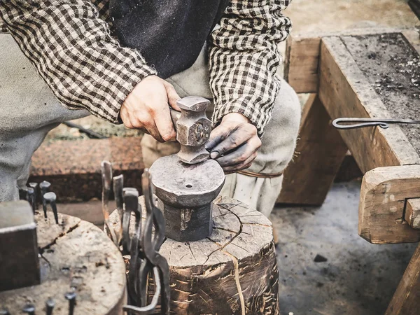 Mano de herrero con un martillo sobre yunque de acero. Mano de herrero con martillo de cerca. El herrero en el proceso de producción de productos metálicos hechos a mano en el taller al aire libre — Foto de Stock