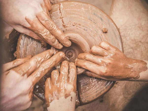 Навчання кераміці Руки карманів, що направляють дитячу руку, показують, як кидати глиняний горщик на гончарне колесо. Концепція вчителя та учня. Вид зверху — стокове фото