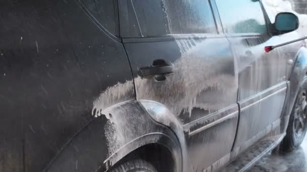 Slow Motion Video of a Car Washing Process on a Self-Service Car Wash. A Jet of Water With a High Pressure Wash Off the Dirt From the Car. Side View. Foamed Detergent Drains From the Surface of the — Stock Video