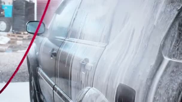 Slow Motion Video av en biltvätt processen på en självbetjäning Car Wash. En vattenstråle med en hög press-tvätta bort smuts från bilen. Sidovy. Skummade tvättmedel avlopp från ytan av den — Stockvideo