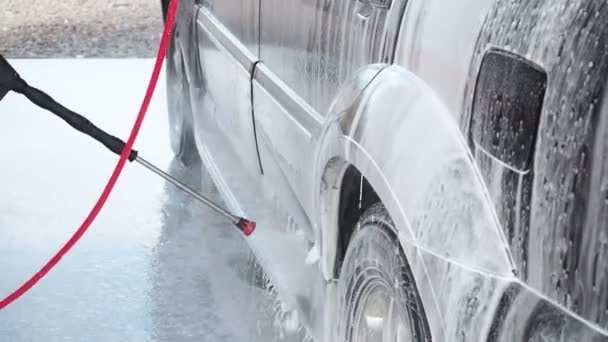 Zeitlupenvideo einer Autowäsche an einer Selbstbedienungswaschanlage. Ein Wasserstrahl mit hohem Druck wäscht den Schmutz vom Auto ab. Seitenansicht. geschäumtes Reinigungsmittel fließt von der Oberfläche des — Stockvideo