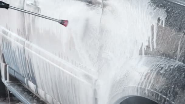 Slow Motion Video of a Car Washing Process on a Self-Service Car Wash. A Jet of Water With a High Pressure Wash Off the Dirt From the Car. Side View. Foamed Detergent Drains From the Surface of the — Stock Video