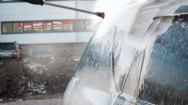 Vidéo au ralenti d'un processus de lavage de voiture sur un lave-auto libre-service.Un jet d'eau avec un lavage à haute pression de la saleté de la voiture. Vue latérale. Drains de détergent mousse de la surface de la — Video