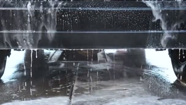 Biltvätt processen på en självbetjäning Car Wash. En vattenstråle med en hög högtryckstvätt bort skummet från den bil bakifrån. Vatten med skum avlopp från stötfångaren på marken. — Stockvideo