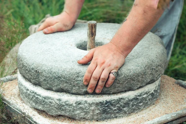 The ancient stone hand grain mill. Mens hands rotate a stone millstone — Stock Photo, Image