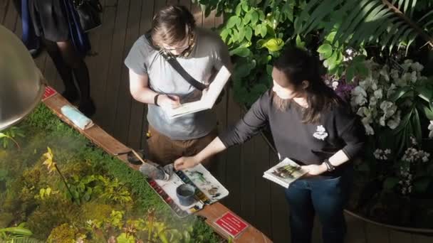 Moskou, Rusland, 17 april 2019: jonge mensen kunsten schilders verf planten met aquarellen in de botanische tuin praten over verschillende onderwerpen te gebaren — Stockvideo
