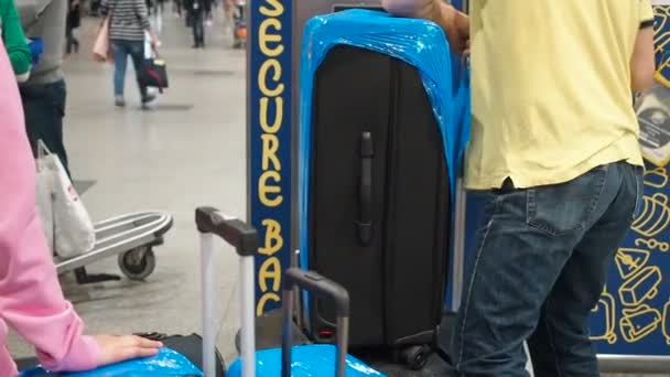 空港での荷物ラッピングサービスは、荷物はセロハン粘着フィルムに詰め込まされています。労働者はプラスチックストレッチフィルムに多数のスーツケースを包んだ — ストック動画