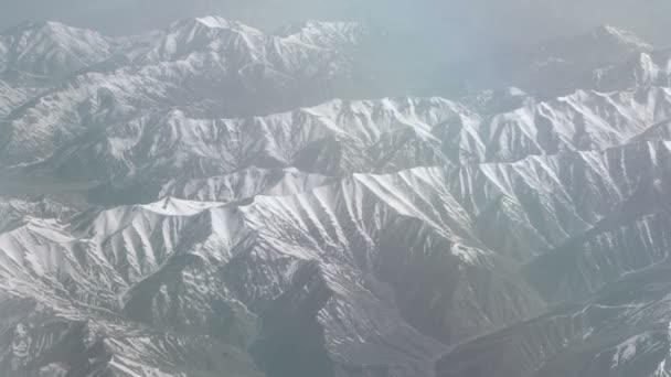 Luftaufnahme von verschneiten Bergen. Blick aus dem Flugzeug auf eine Gebirgsfalte. die Gipfel der schneebedeckten Berge aus dem Fenster des Flugzeugs. alborz oder alburz, elburz oder elborz — Stockvideo
