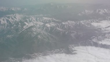 Karlı dağların ve bulutların havadan görünümü. Bir dağ kıvrımları üzerinde düzlemden görünümü. Dağların tepesi uçağın penceresinden karla kaplıydı. Alborz veya Alburz, Elburz veya Elborz