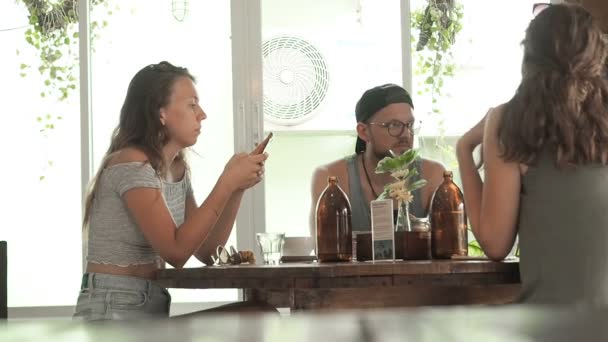 Diverse studerende sidder ved bordet i cafe og taler om noget. Møde venligt selskab ved et bord i en cafe over en kop kaffe. Unge mennesker bruger tid i en kaffebar chatter og – Stock-video