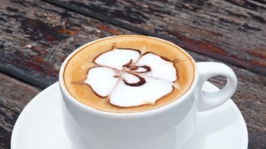 Tahta rustik masada kaşıkla tabakta beyaz fincan aromalı kahve, dalga hareketi. Tropik bir tesiste deniz manzaralı kahve içmek. Aromalı kapuçino sabah fincan rüzgarda sallanan