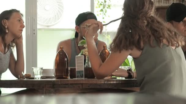 Koh phangan, thailand - 23. Mai 2019: Diverse Studenten sitzen um einen Tisch im Café und reden über etwas und lächeln. Bei einer Tasse Kaffee trifft man sich in geselliger Runde an einem Tisch in einem Café. jung — Stockvideo