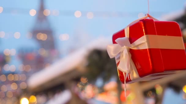 Anno nuovo e scenario stradale di Natale della città europea. La confezione regalo decorativa legata con un nastro bianco satinato ruota su una corda sospesa all'abete rosso sullo sfondo di una luminosa illuminazione — Video Stock