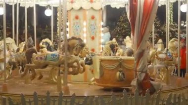 Moskova - 25 Aralık 2018 Kar yağarken Noel tatili sırasında bir çocuk atlıkarıncaya biniyor. Işıklı kavşak çocuklarla birlikte döner. Küçük çocuk parlayan neşeli üzerinde sürmek yuvarlak gitmek