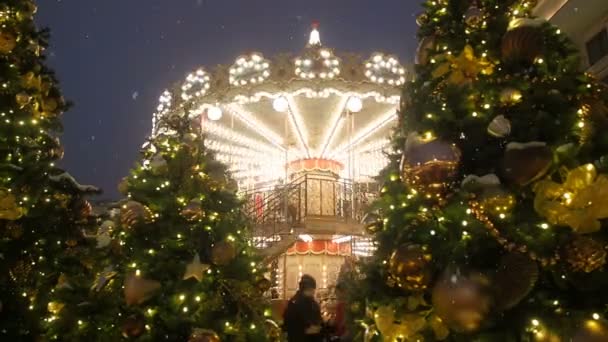 Beautiful brightly glowing carousel decorated and arranged for Christmas and New Year. Christmas fairy illuminated turnabout rotates during snowfall. Luminous roundabout spinning. Wonderful magic xmas — Stock Video