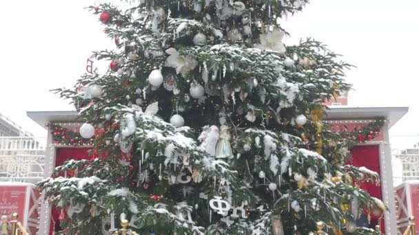Kamerafahrt von unten nach oben mit Fokus auf den großen Weihnachtsbaum, der mit Schnee bedeckt ist und wunderschönen Dekorationen aus farbigen Kugeln, Ornamenten und leuchtenden Girlanden mit verschiedenen Buchstaben des — Stockvideo