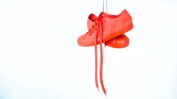 Coppia di scarpe da ginnastica rosse da donna appese su sfondo bianco. Bright Coral Womans Trainers Uscire sulla corda. Concetto minimalista — Video Stock