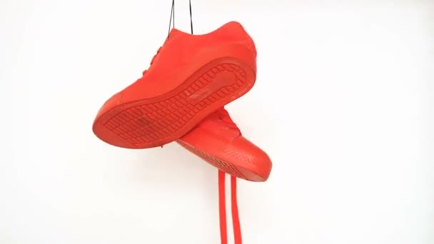 Coppia di scarpe da ginnastica rosse appese su sfondo bianco. Stivali arancioni che girano sulla corda — Video Stock