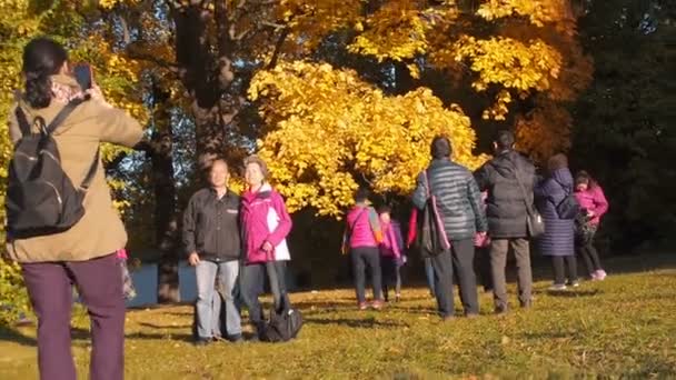 Mosca, Russia - 11 ottobre 2018: i turisti cinesi camminano nel parco autunnale. Gli asiatici scattano foto sullo sfondo di un bellissimo acero ingiallito nel parco autunnale. Giornata di sole nel parco cittadino — Video Stock