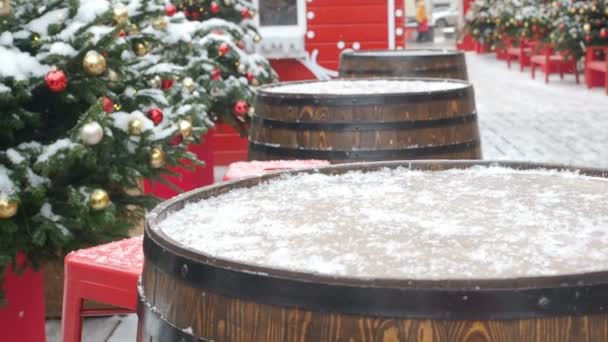 Pohyb kamery zdola nahoru se změnou zaměření z dubových sudů na barevné koule visící na vánočním stromku pokrytých sněhem a červeným perníku. Krásná dekorovaná ulice pro — Stock video