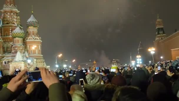 Moscú, Rusia - 1 de enero de 2019: Mucha gente se reunió para una celebración universal de Año Nuevo en Moscú. Fuegos artificiales en la Plaza Roja cerca de la Torre Spasskaya en la víspera de Año Nuevo. Multicolor saludo en el — Vídeos de Stock