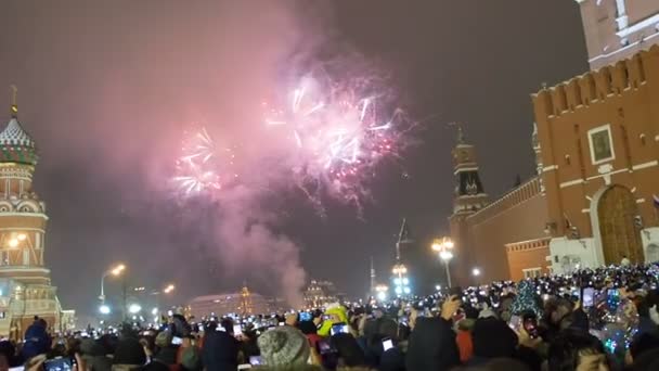 Moscú, Rusia - 1 de enero de 2019: Mucha gente se reunió para una celebración universal de Año Nuevo en Moscú. Fuegos artificiales en la Plaza Roja cerca de la Torre Spasskaya en la víspera de Año Nuevo. Multicolor saludo en el — Vídeo de stock