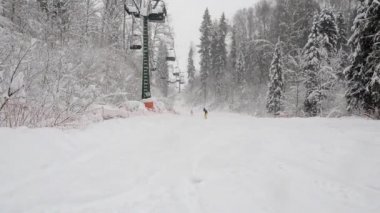 Kış karlı ormanlarda kayak pistinde iki koltuklu bir teleferiğin alt manzarası. Bir kar yağışı sırasında Stepanovo kayak merkezindeki kayak pistinin tepesine tırman. İnsanlar kayak ve snowboard yapmaya gider.