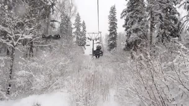 Flygfoto över en två-sits linbana över vintern snöig skog. Sittliften klättrar över skidbacken i lilla skidorten Stepanovo under snöfall — Stockvideo