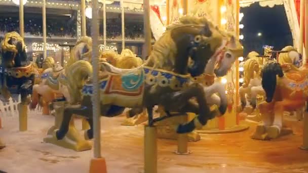 Carousel during the Christmas holidays while the snow falls. Luminous roundabout rotates on the street. Glowing merry go round in snowy weather — Stock Video