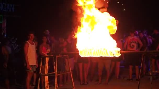 Koh Phangan, Thailand, May 19, 2019: A cheerful youth dancing the dance of Limbo at nighttime. Young girl bends pass under the burning crossbeam on a beach full moon party. Group of people playing — Stock Video