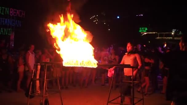 Koh Phangan, Thailand, May 19, 2019: A cheerful youth dancing the dance of Limbo at nighttime. Young boy bends pass under the burning crossbeam on a beach full moon party. Group of people playing — Stock Video