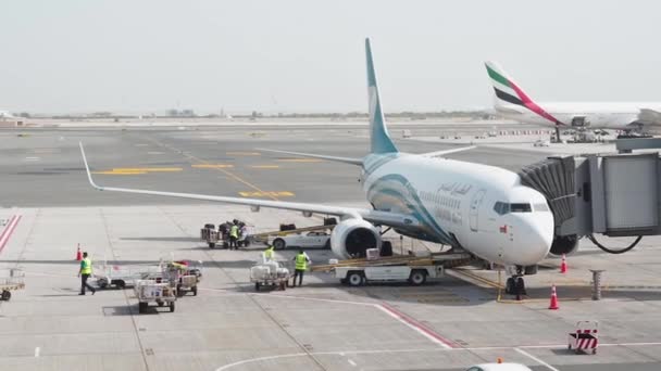 Muscat, Oman - 6 Mei 2019: Memuat bagasi dalam pesawat. Pekerja laki-laki mengangkut bagasi penumpang ke kargo pesawat dari maskapai penerbangan Oman Air. Koper bergerak di sepanjang ban berjalan. — Stok Video