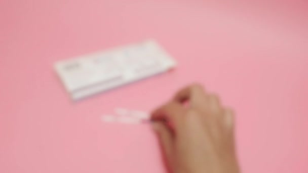 Женщина держит положительный тест на беременность на розовом фоне. Сокращение HCG на синей полосе означает, что хорионический гонадотропин человека является гормоном, вырабатываемым клетками, которые окружают — стоковое видео