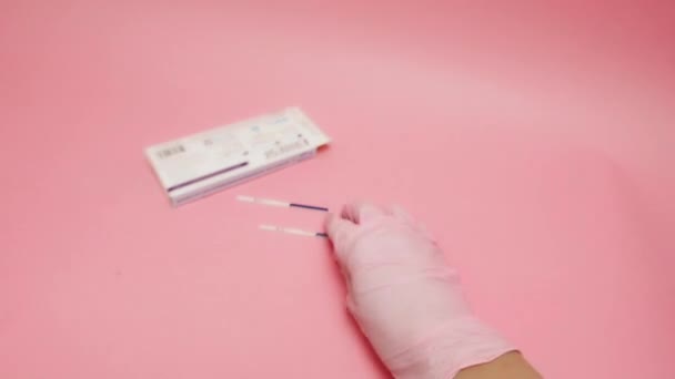 Ręka kobiety w różowej rękawicy medycznej z dodatnim wynikiem testu ciążowego i pokazywaniem gestu kciuka w górę odizolowanego na różowym tle. Skrót HCG na niebieskim pasku oznacza ludzką gonadotropinę kosmówkową. — Wideo stockowe