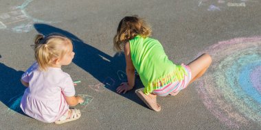İki küçük kız asfalta tebeşir çiziyor.