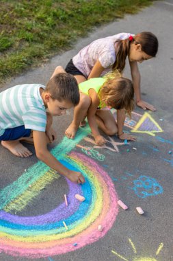 Çocuklar asfalta tebeşirle resim çizerler. Gökkuşağı, ev, güneş, bulutlar asfalta çizilmiş..