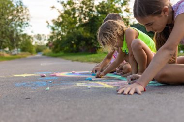 Çocuklar asfalta tebeşirle resim çizerler. Gökkuşağı, ev, güneş, bulutlar asfalta çizilmiş..