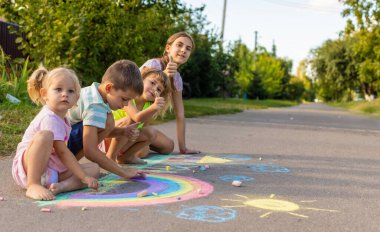 Çocuklar asfalta tebeşirle resim çizerler. Gökkuşağı, ev, güneş, bulutlar asfalta çizilmiş..