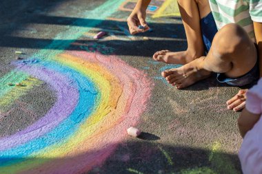 Tebeşirle çizen çocuk gökkuşağı ve asfaltta bir ev.