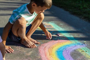 Tebeşirle çizen çocuk gökkuşağı ve asfaltta bir ev.