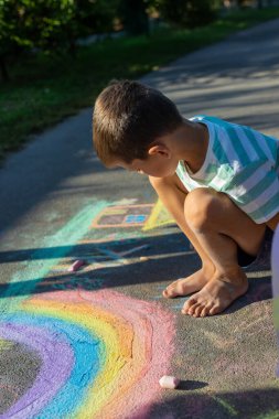 Tebeşirle çizen çocuk gökkuşağı ve asfaltta bir ev.